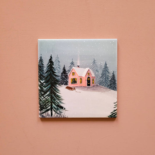 Een illustratie van een winterhuisje op een decoratief tegeltje.