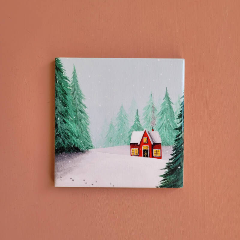 Een illustratie van een rood winterhuisje op een keramieken tegeltje.