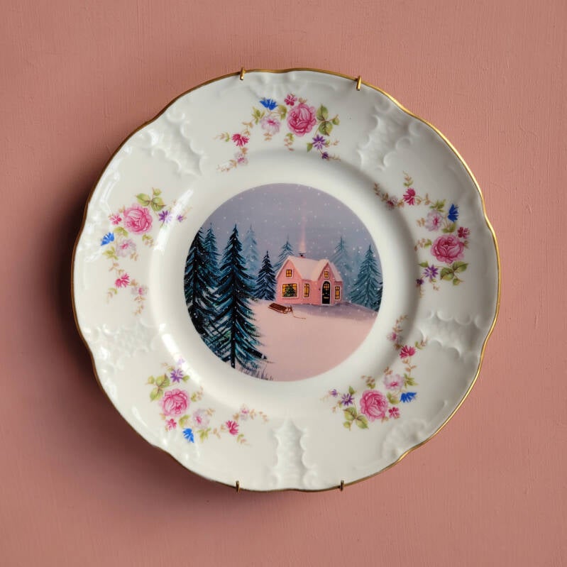 Een illustratie van een roze winterhuisje op een decoratief wandbord.